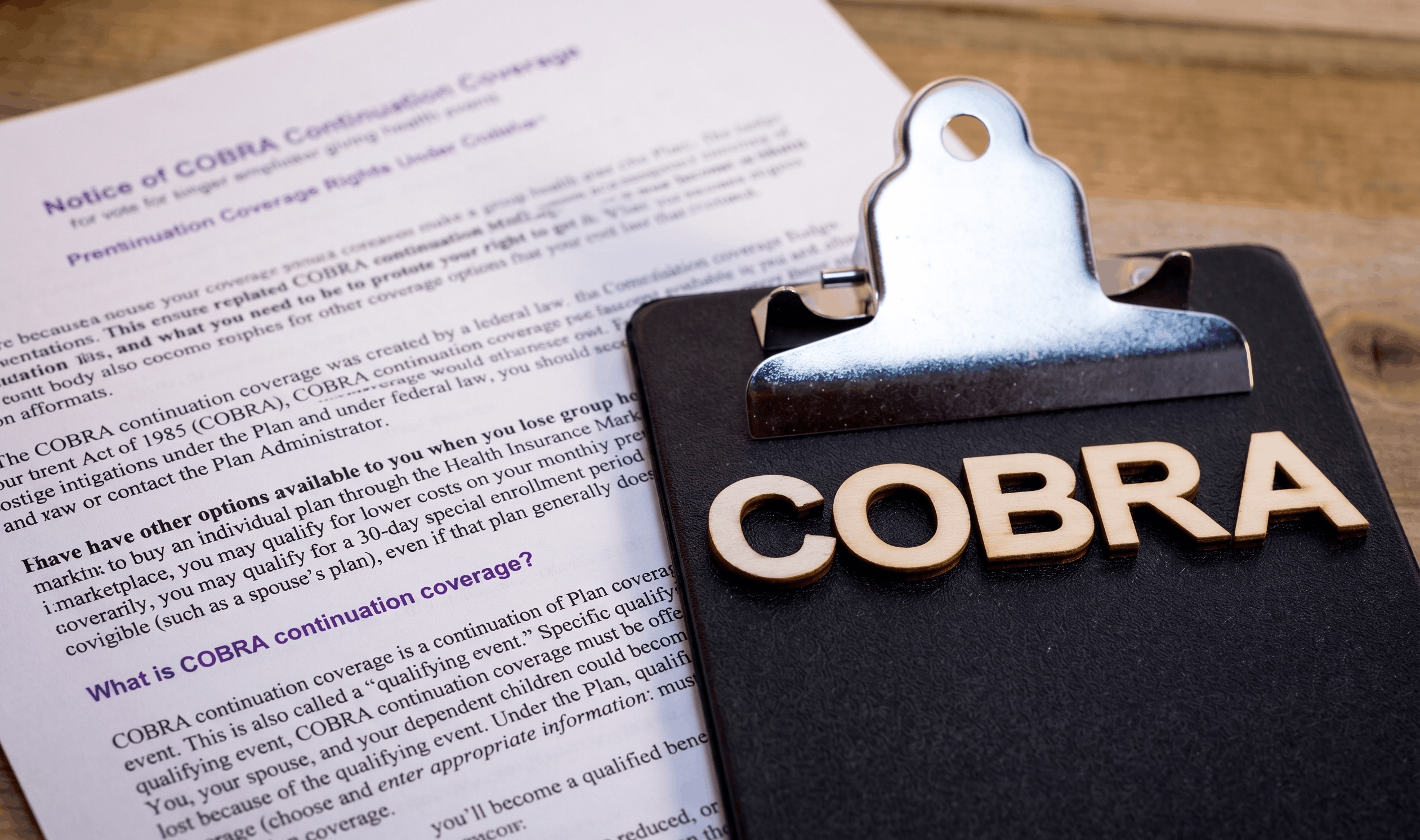 Clipboard with wooden letters spelling COBRA next to a document about COBRA continuation coverage.