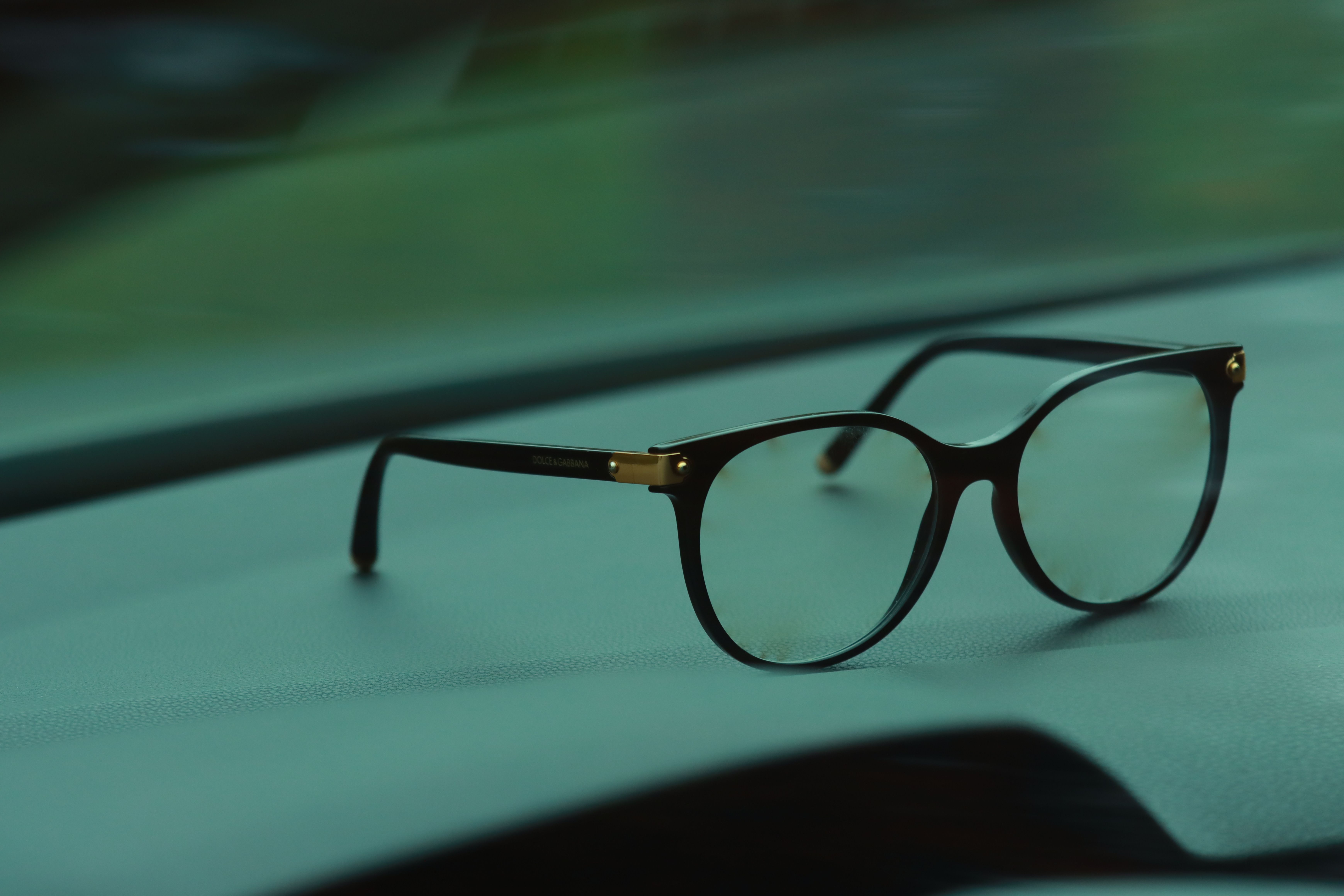 Black and gold Dolce & Gabbana eyeglasses resting on a smooth teal surface.