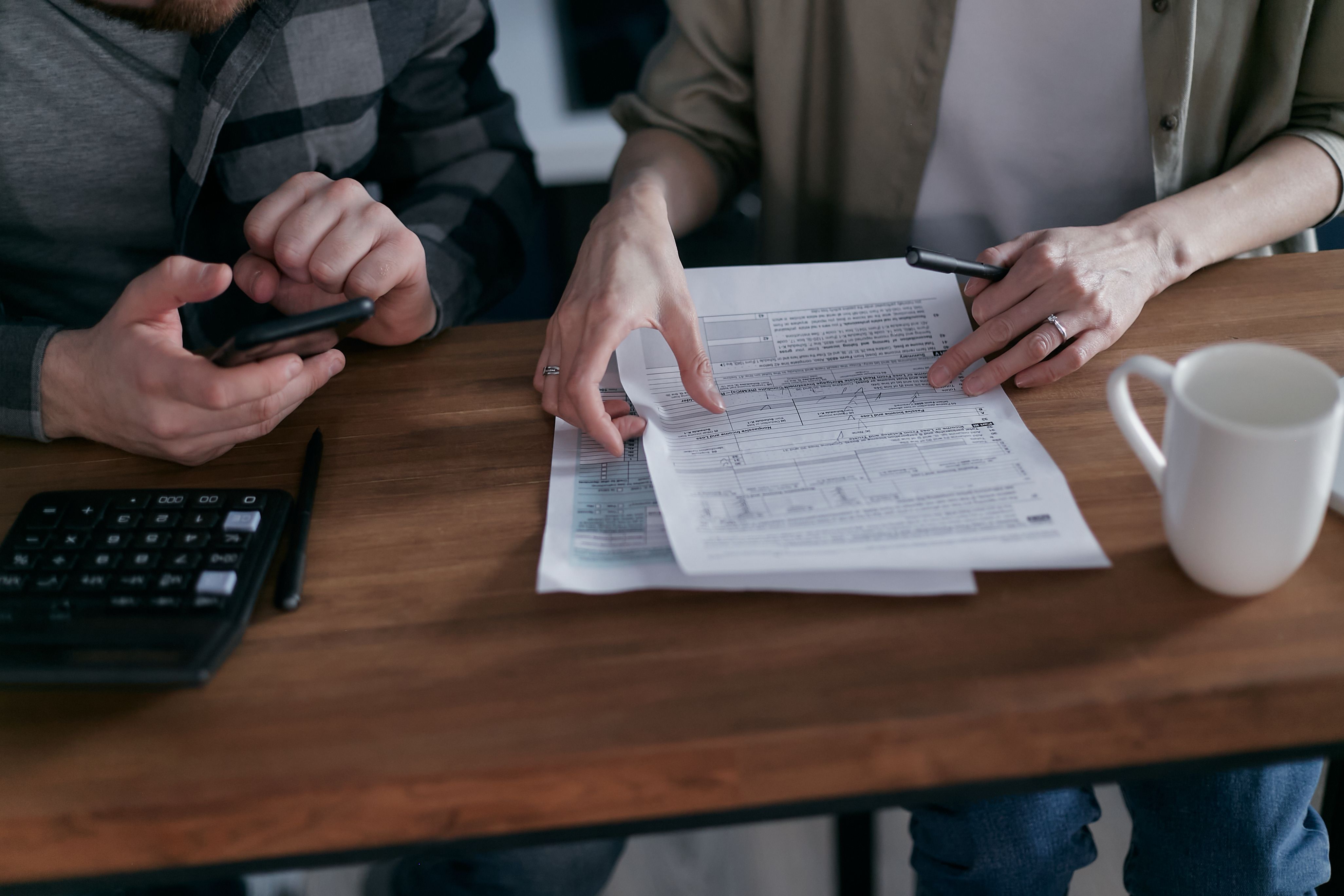 Couple reviewing financial documents at a wooden table with a calculator and a coffee mug.