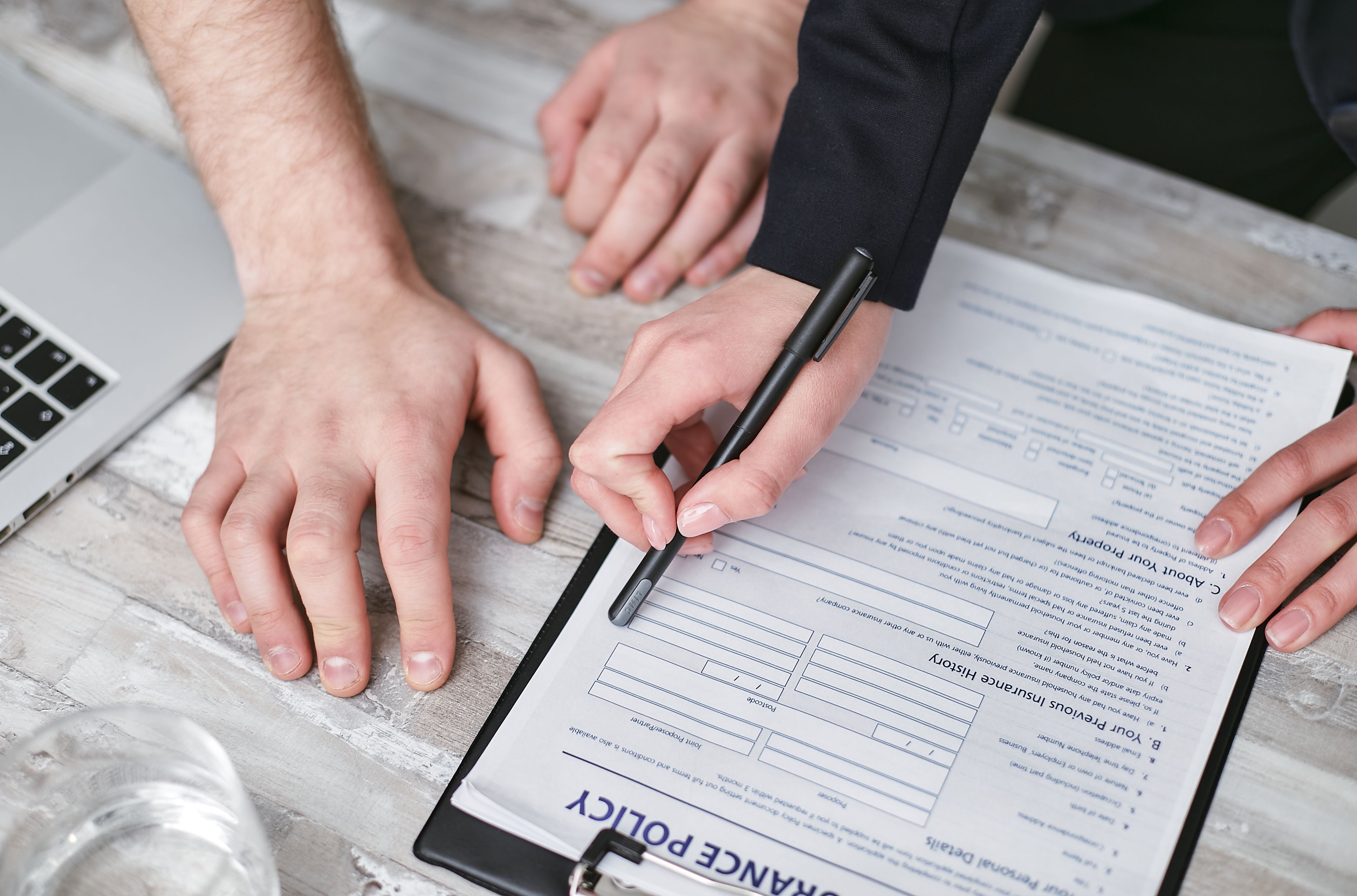 Hands of two people reviewing and filling out an insurance policy document on a clipboard.