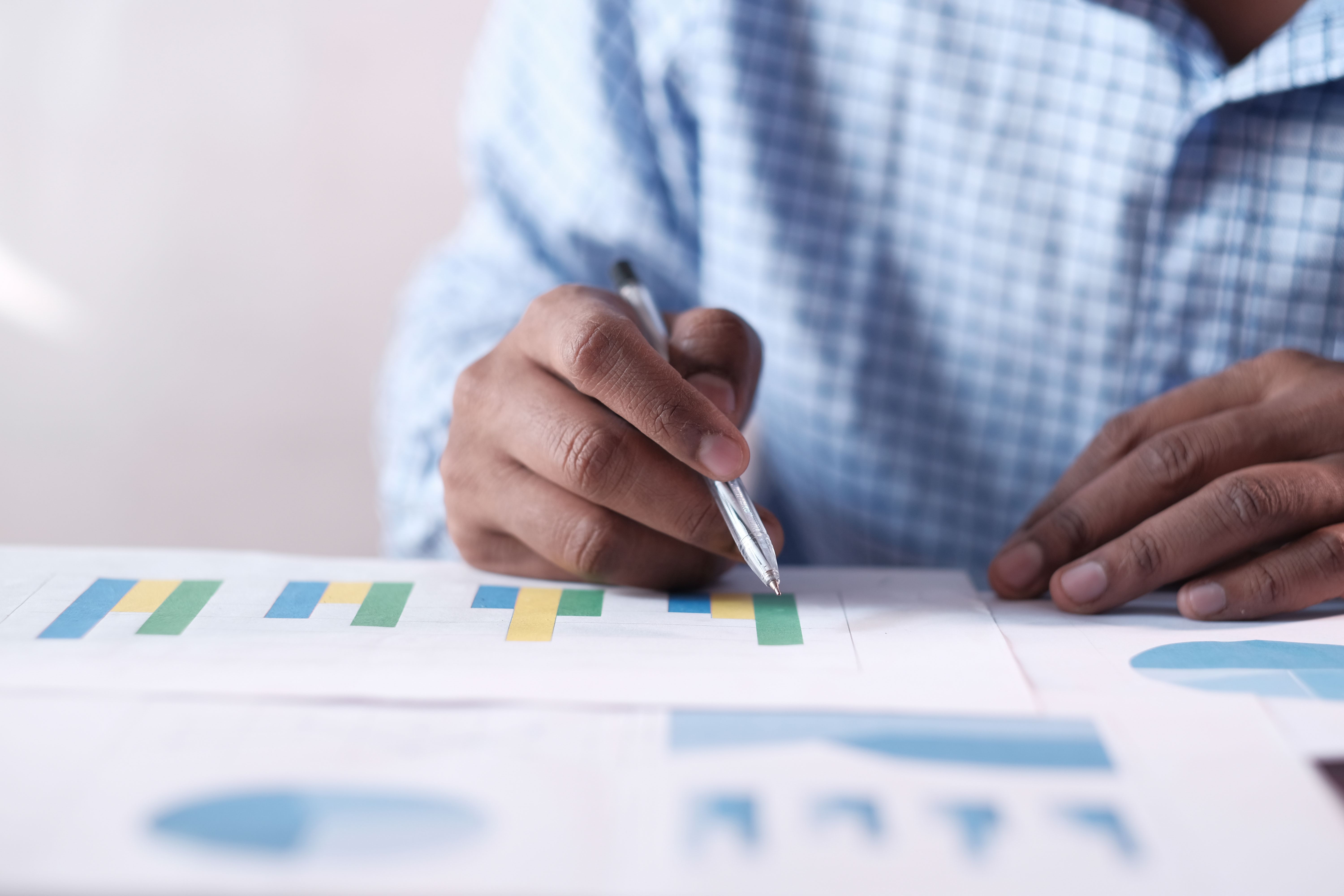 Person in blue checkered shirt marking colorful bar charts with a pen on paper.